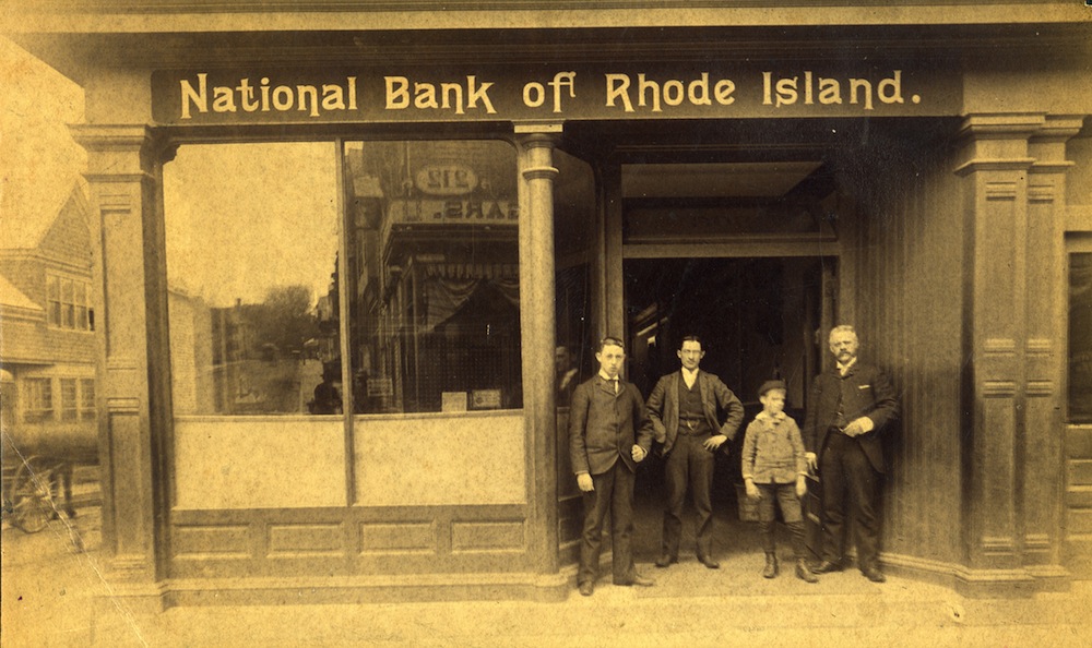 A sepia tone photograph of Arthur H. Popple, John Peckham, an unidentified boy, and Thomas Peckham standing ouside the National Bank of Rhode Island, c. 1890. © Newport Historical Society. Reprinted with permission.